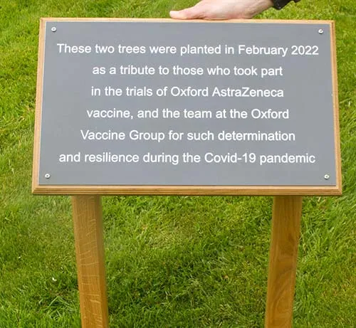 A grey composite with white letters on a wooden backiing board with posts. Grey Composite Sign