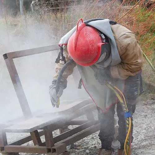 Large objects are sand blasted outside. Sandblaster At Work